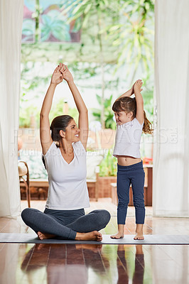Buy stock photo Shot of a focused young mother and daughter doing a yoga pose together with their arms raised above their heads