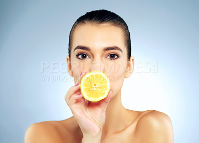 Buy stock photo Studio portrait of a beautiful young woman covering her mouth with a lemon against a blue background