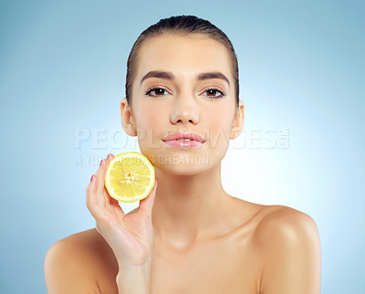 Buy stock photo Studio portrait of a beautiful young woman holding a lemon against a blue background