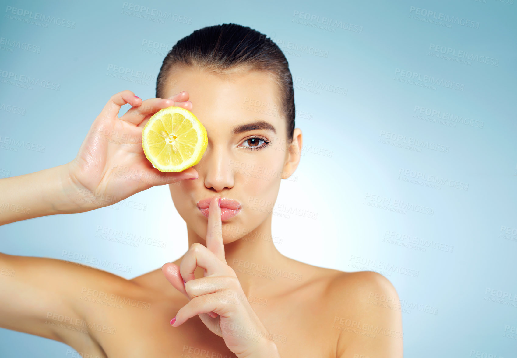 Buy stock photo Studio portrait of a beautiful young woman covering her eye with a lemon and putting her finger to her lips