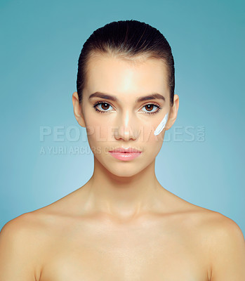 Buy stock photo Studio portrait of a beautiful young woman with moisturizer on her cheek against a blue background