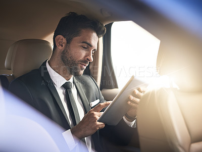 Buy stock photo Cropped shot of a handsome young businessman using a tablet while on his morning commute to work
