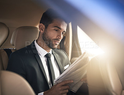 Buy stock photo Cropped shot of a handsome young businessman reading the paper while on his morning commute to work