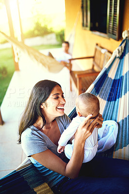 Buy stock photo Shot of a cheerful young mother holding her baby infant son while smiling at him outside at home