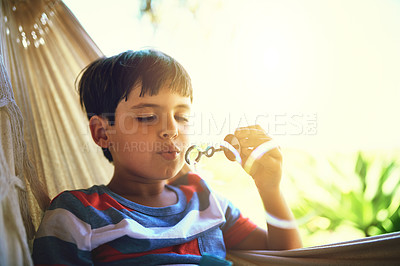 Buy stock photo Shot of a curious little boy blowing bubbles while being seated outside at home during the day