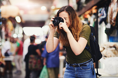 Buy stock photo Shot of a focused young woman taking photos of market stalls at a busy bazaar outside during the day