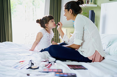 Buy stock photo Shot of a mother and her little daughter playing with makeup on the bed at home