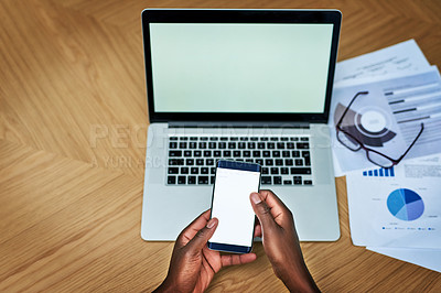 Buy stock photo High angle shot of an unrecognizable businessperson texting on their cellphone while working on a laptop at a desk
