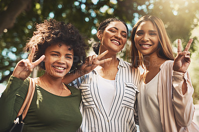 Buy stock photo Portrait of a cheerful young group of friends standing together while showing the peace sign outside during the day