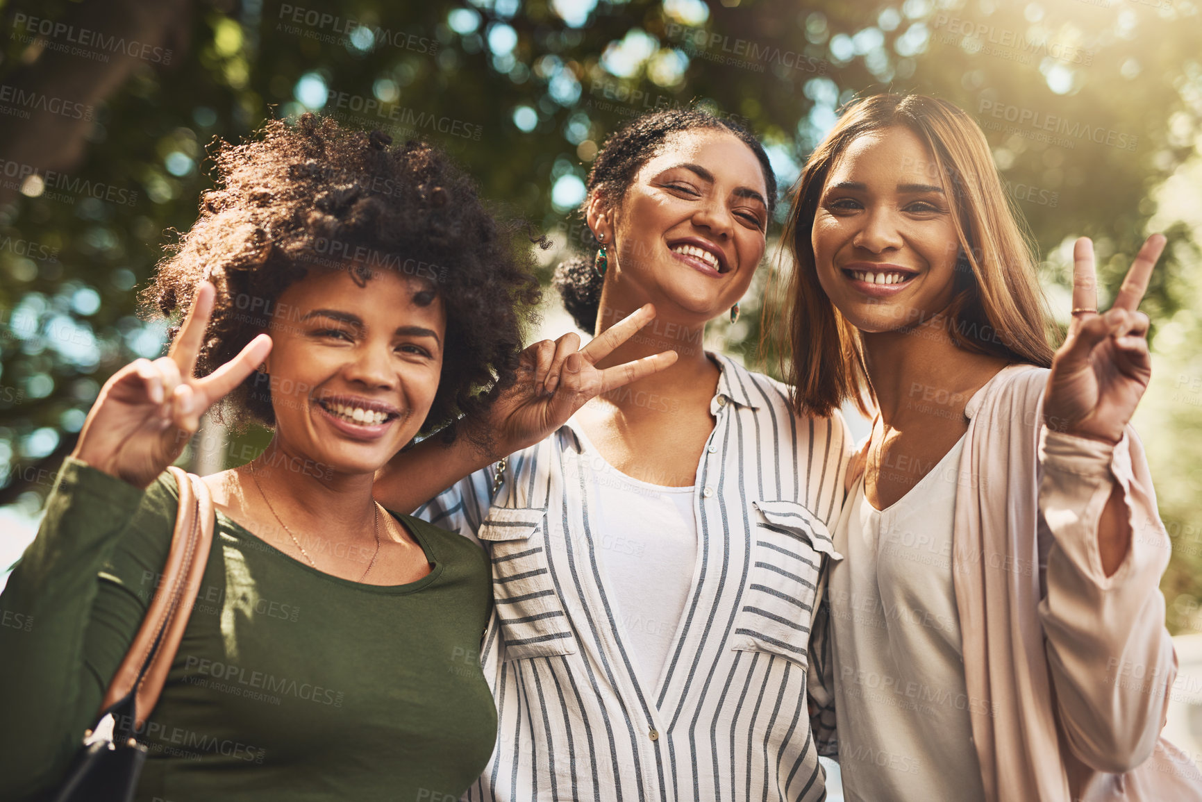 Buy stock photo Portrait of a cheerful young group of friends standing together while showing the peace sign outside during the day