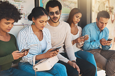 Buy stock photo Shot of a group of focused young friends seated next to each other while texting and browsing on their cellphones outside during the day