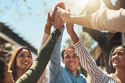 Buy stock photo Shot of a group of cheerful young friends forming a huddle and giving each other a high five outside during the day