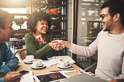 Buy stock photo Shot of two cheerful young work colleagues shaking hands after an successful meeting at a coffeeshop during the day