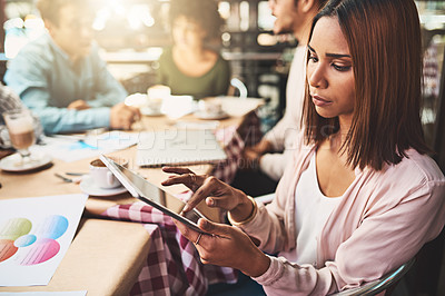 Buy stock photo Shot of a focused young woman browsing on a digital tablet while being seated next to a table at a coffeeshop