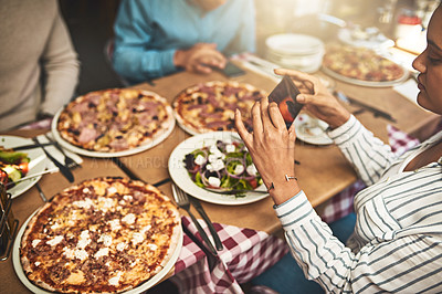 Buy stock photo Shot of a group of people seated at a table with plates of pizza in front of them while one takes a photo of it inside of a restaurant