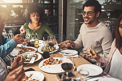 Buy stock photo Shot of a group of cheerful young friends eating pizza together while being seated at a table inside of a restaurant