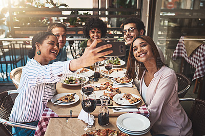 Buy stock photo Shot of a group of cheerful young friends taking a self portrait together with a cellphone while being seated at a table inside of a restaurant