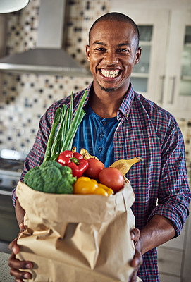 Buy stock photo Cropped portrait of a handsome young man holding a bag of groceries in the kitchen at home