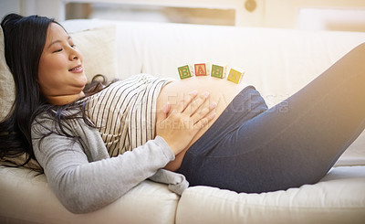 Buy stock photo Shot of an attractive young pregnant woman balancing wooden blocks on her tummy while relaxing on the sofa at home