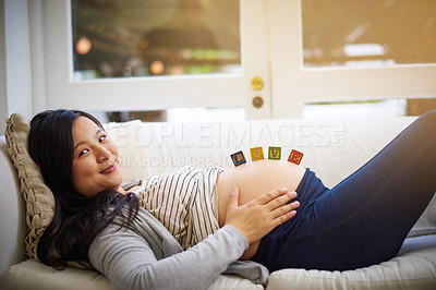 Buy stock photo Portrait of an attractive young pregnant woman balancing wooden blocks on her tummy while relaxing on the sofa at home
