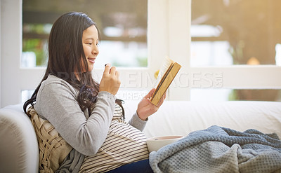 Buy stock photo Cropped shot of an attractive young pregnant woman eating fruit and reading a book while relaxing on the sofa at home