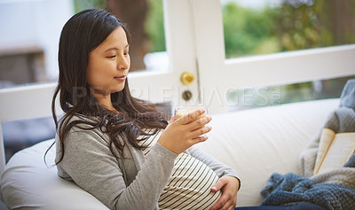 Buy stock photo Shot of an attractive young pregnant woman drinking an iced coffee while relaxing on the sofa at home