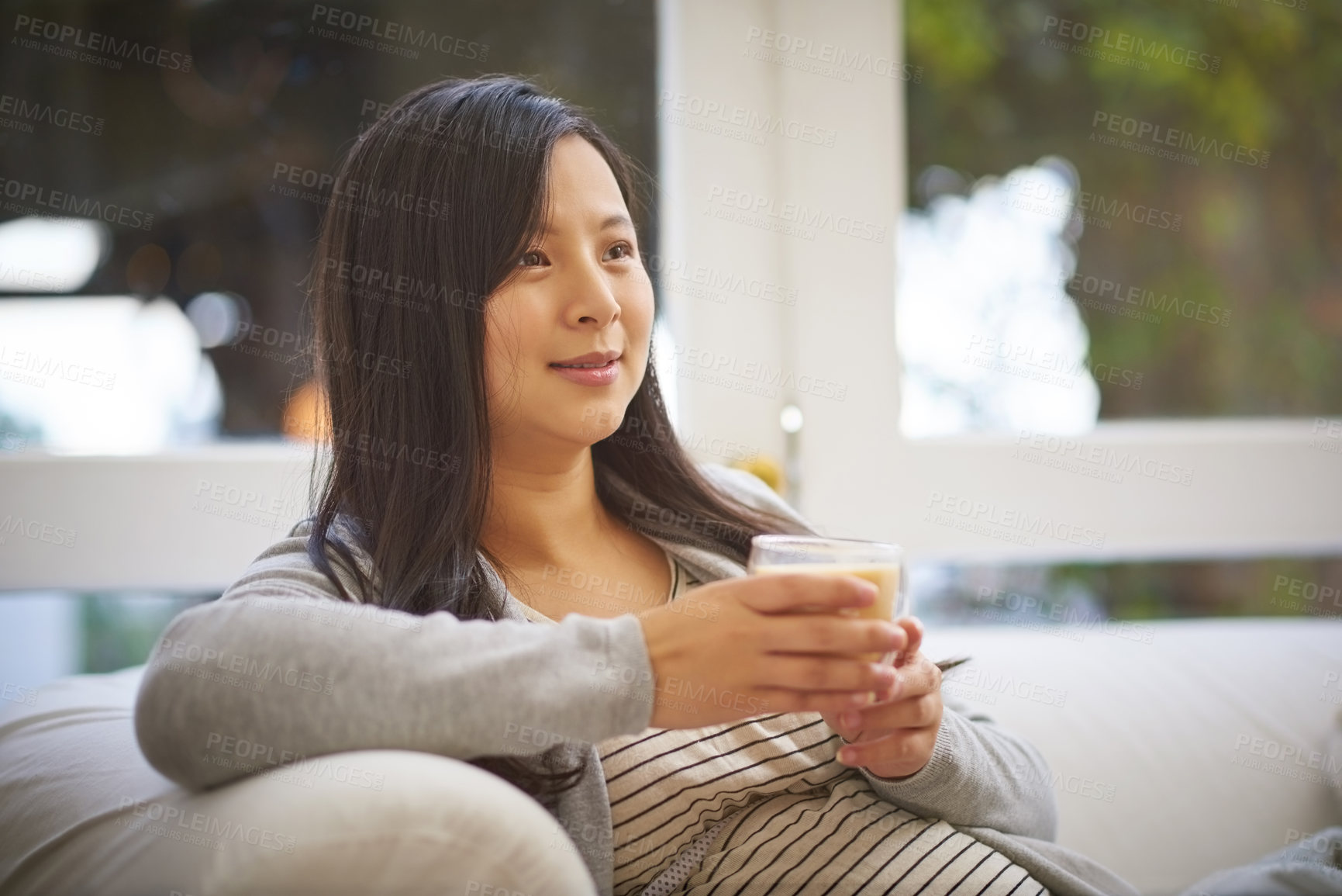 Buy stock photo Shot of a pregnant woman looking thoughtful while drinking a warm beverage at home