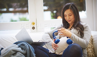 Buy stock photo Cropped shot of an attractive young pregnant woman holding headphones to her tummy while relaxing on the sofa at home