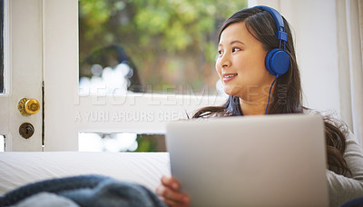 Buy stock photo Shot of an attractive young woman wearing headphones while using a laptop at home