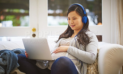 Buy stock photo Shot of a pregnant woman wearing headphones while using a laptop at home