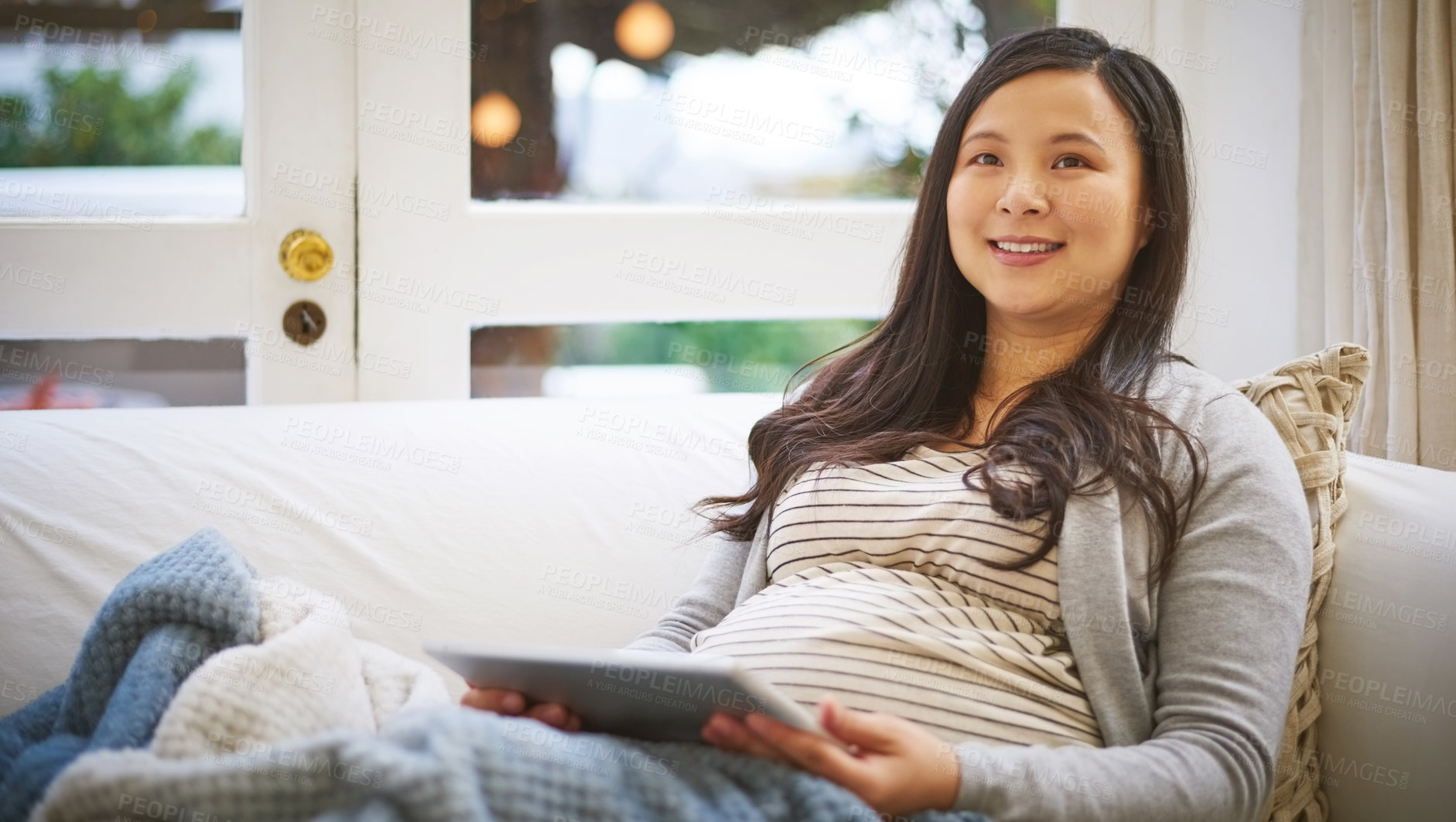 Buy stock photo Shot of a pregnant woman looking thoughtful while using a digital tablet at home