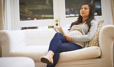 Buy stock photo Shot of a pregnant woman looking thoughtful while reading a book at home