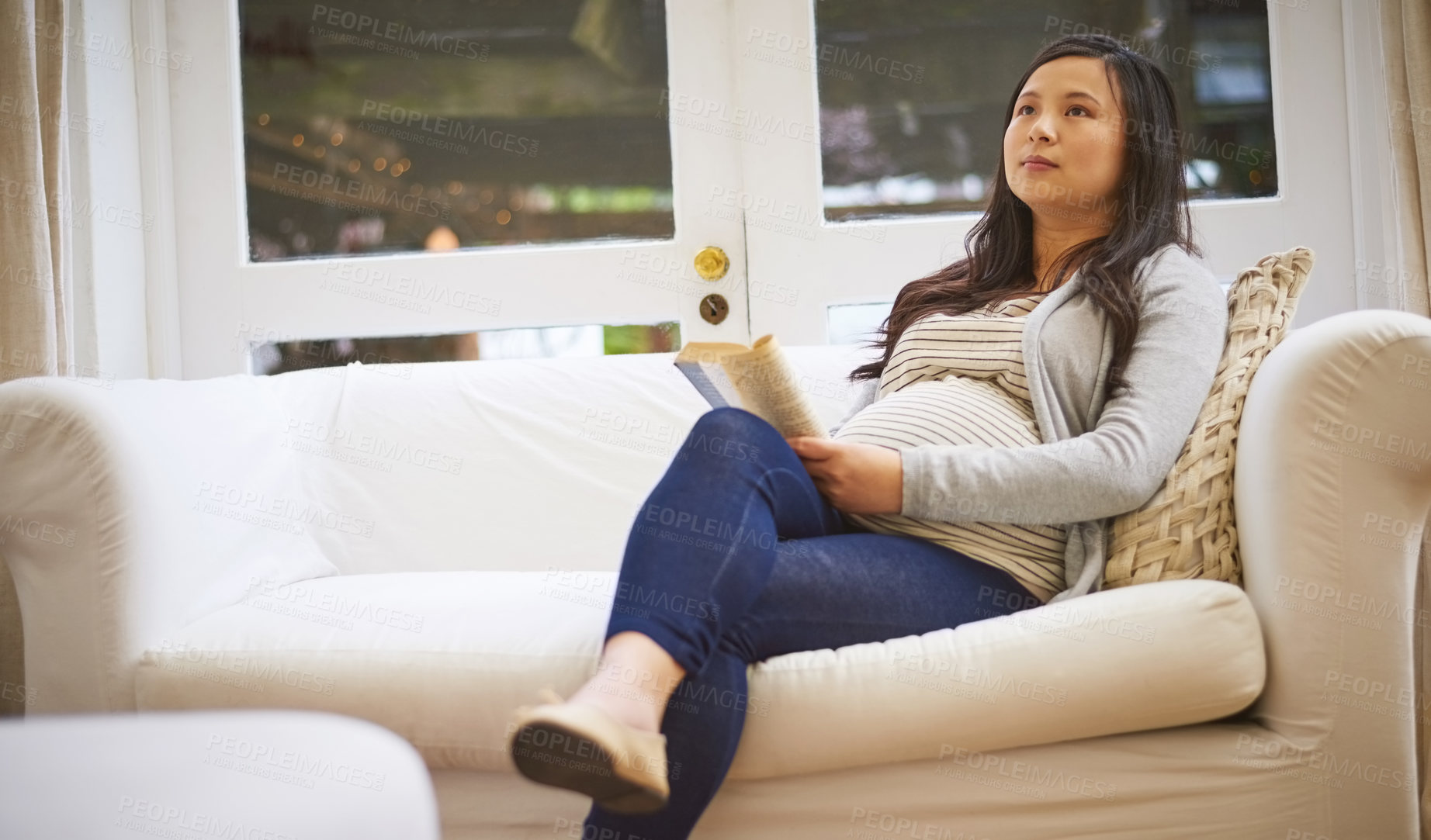 Buy stock photo Shot of a pregnant woman looking thoughtful while reading a book at home