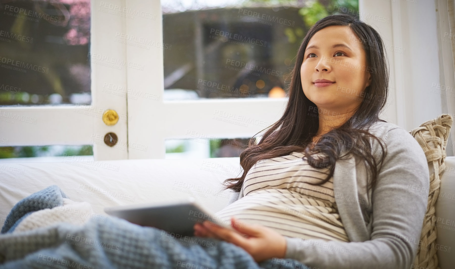 Buy stock photo Shot of a pregnant woman looking thoughtful while using a digital tablet at home