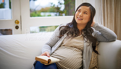 Buy stock photo Shot of a pregnant woman looking thoughtful while reading a book at home