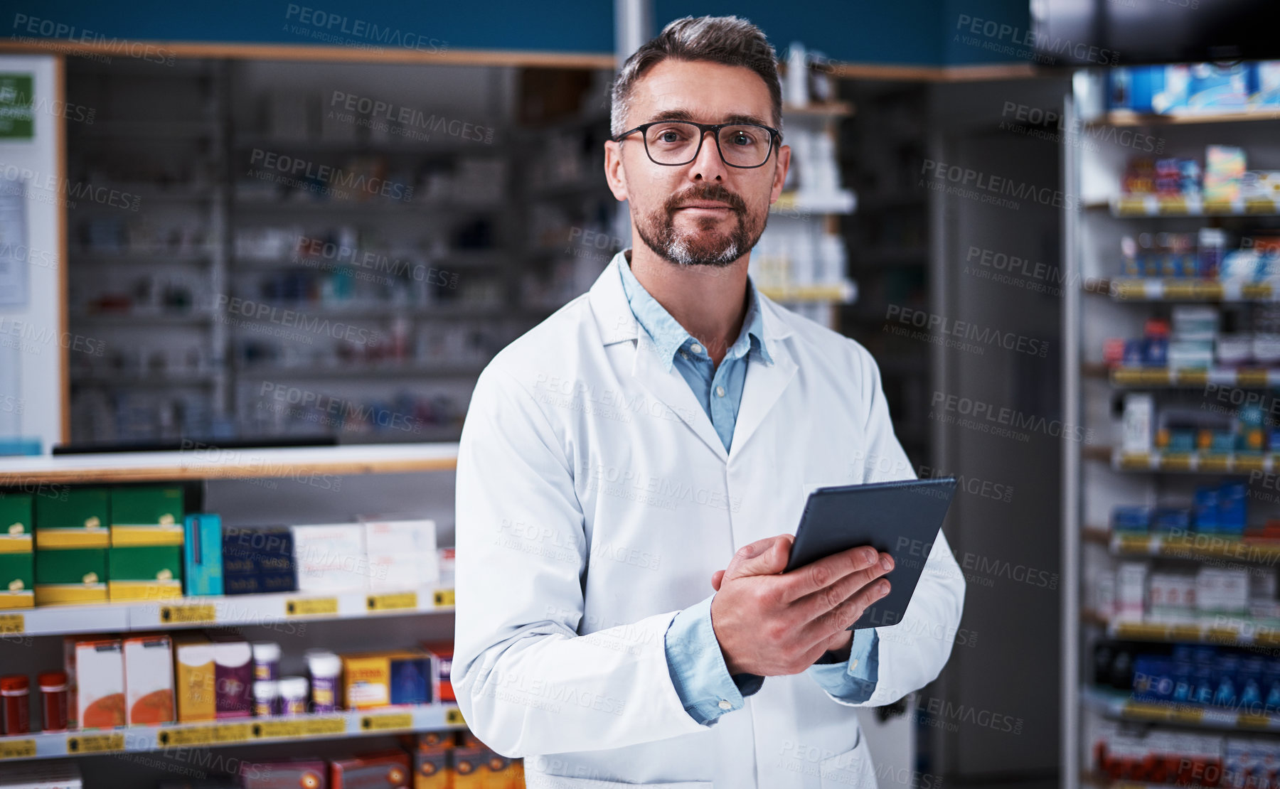 Buy stock photo Portrait of a handsome mature pharmacist using a digital tablet in a pharmacy