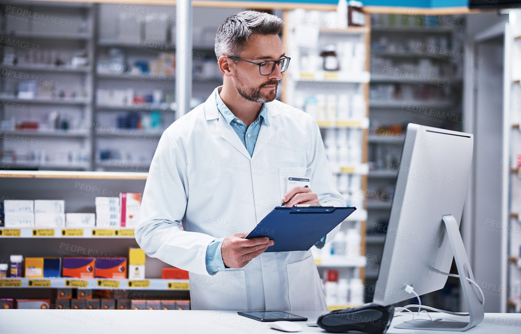 Buy stock photo Shot of a mature pharmacist writing on a clipboard in a pharmacy