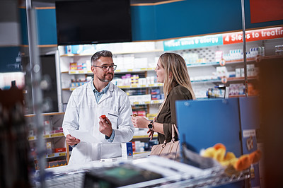 Buy stock photo Shot of a mature pharmacist assisting a young woman in a chemist