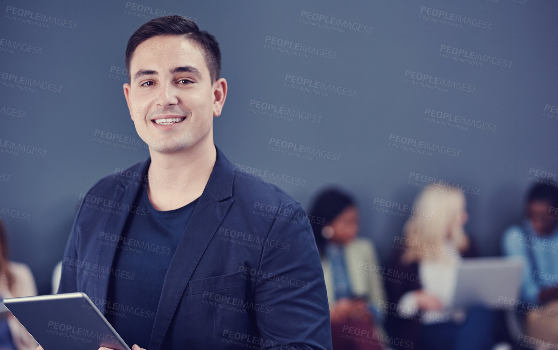 Buy stock photo Cropped portrait of a handsome young businessman using a tablet with his colleagues in the background