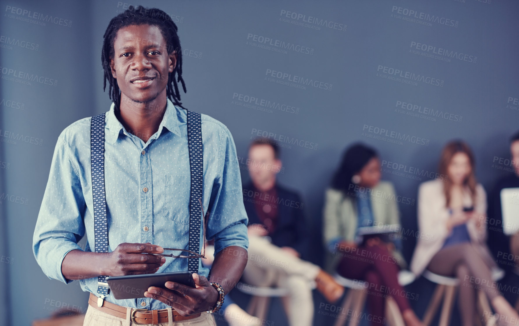 Buy stock photo Cropped portrait of a handsome young businessman using a tablet with his colleagues in the background