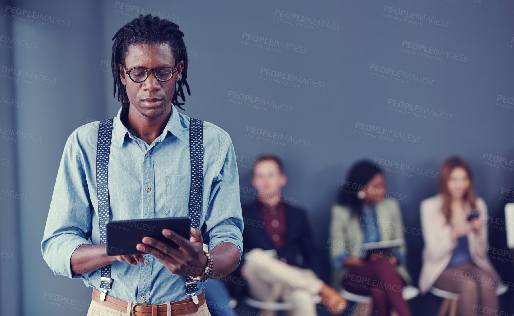 Buy stock photo Cropped shot of a handsome young businessman using a tablet with his colleagues in the background