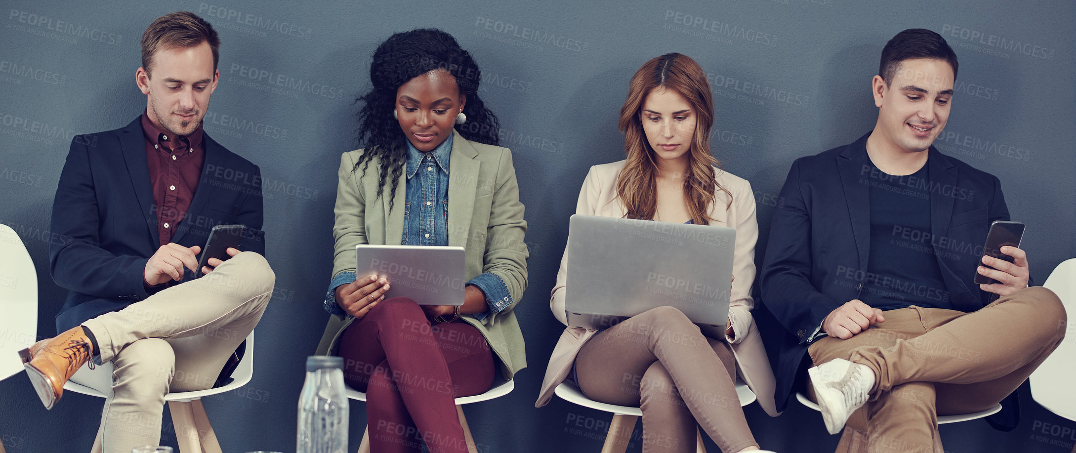 Buy stock photo Shot of a group of businesspeople using different wireless devices while waiting in line for an interview