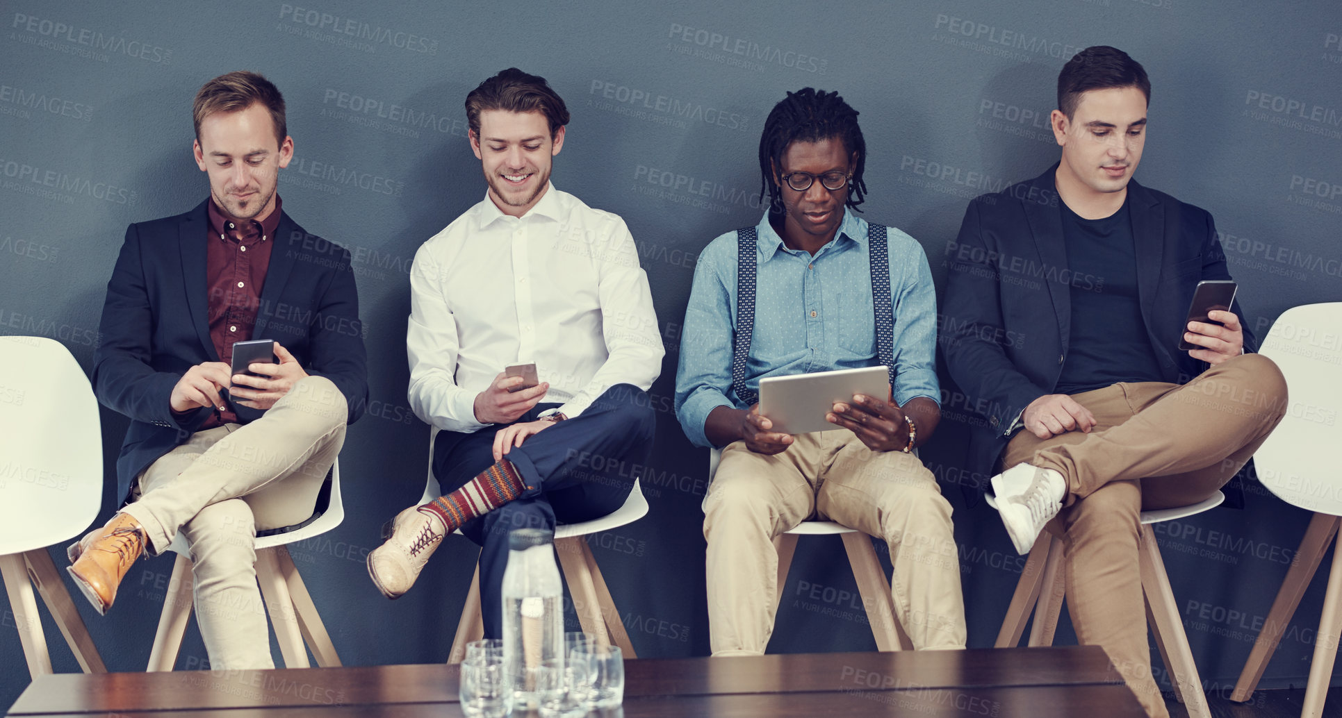 Buy stock photo Shot of a group of businessmen using different wireless devices while waiting in line for an interview