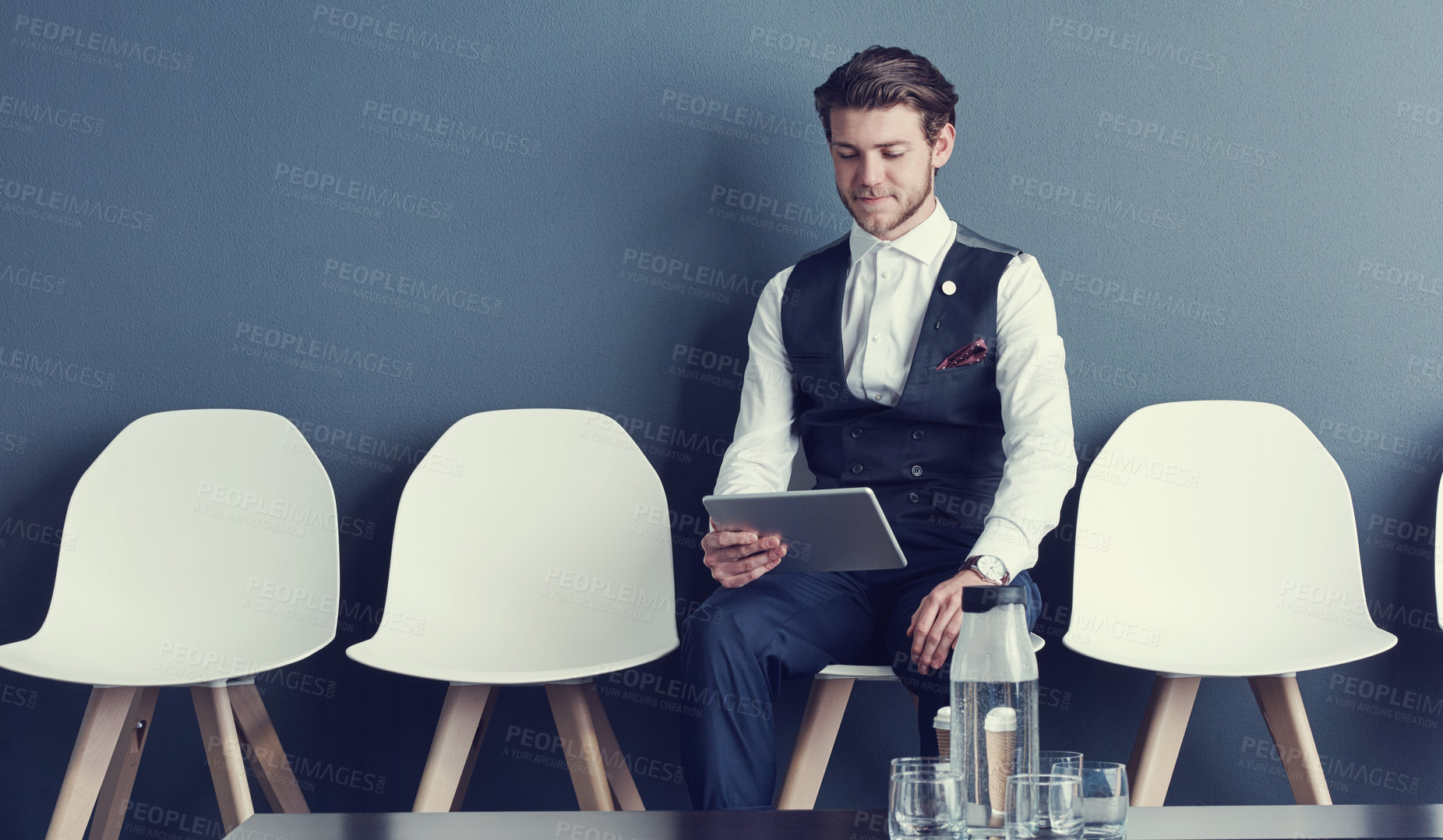 Buy stock photo Shot of a young businessman using a tablet while waiting for an interview