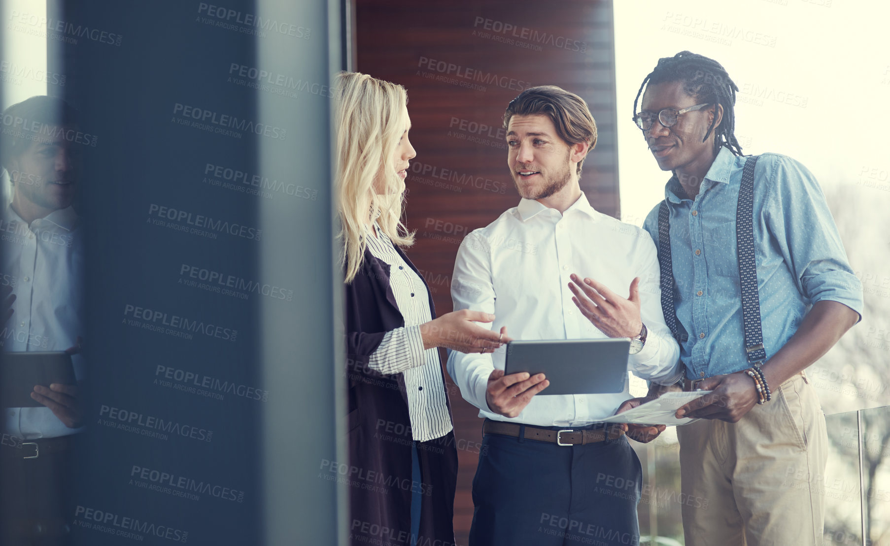 Buy stock photo Cropped shot of three young businesspeople using a tablet while standing outside on the office balcony