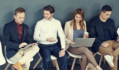 Buy stock photo Shot of a group of businesspeople using different wireless devices while waiting in line for an interview