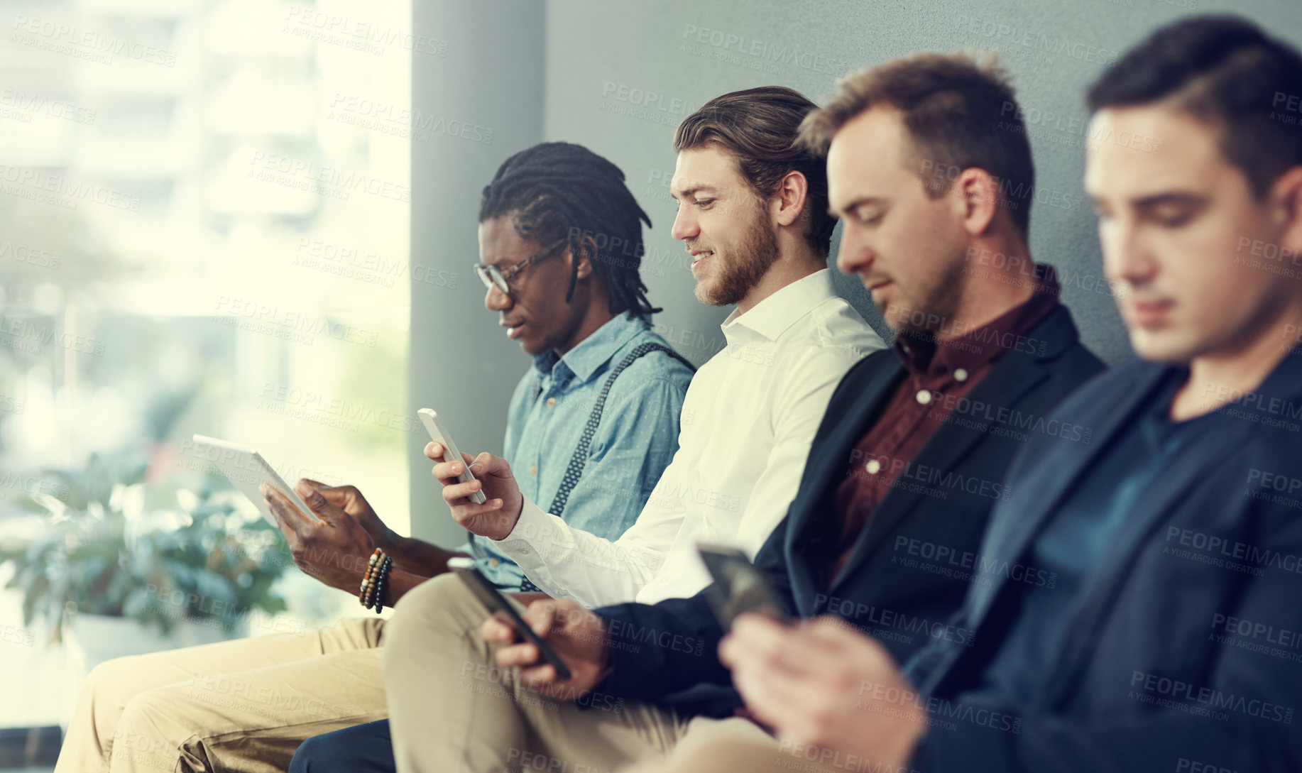 Buy stock photo Shot of a group of businessmen using different wireless devices while waiting in line for an interview