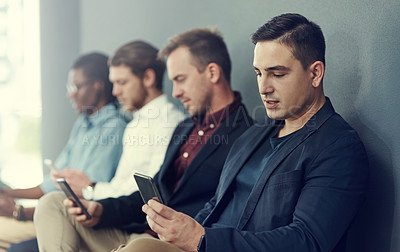 Buy stock photo Shot of a group of businessmen using different wireless devices while waiting in line for an interview