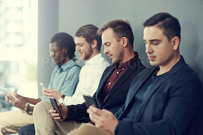 Buy stock photo Shot of a group of businessmen using different wireless devices while waiting in line for an interview