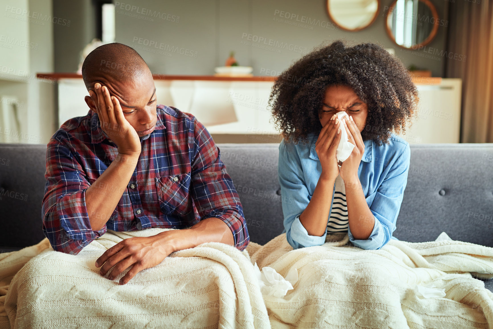 Buy stock photo Shot of a tired looking young couple seated on a couch with blankets while being sick together at home